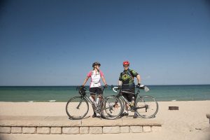 Cyclists taking a break on Lake Michigan on beautiful sandy beaches, with turquoise water and blue sky behind them.