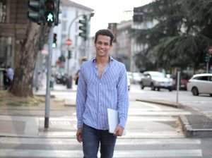 Man smiling, walking across a street holding a laptop