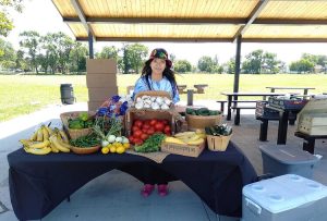 Woman behind table of fruits and vegetables